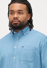 Jasnoniebieska jeansowa koszula na guziki z kołnierzykiem, kieszenią na piersi i dyskretnym logo. Miękka w dotyku, o casualowym kroju.