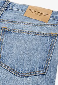 Un bolsillo de jeans de denim azul claro con costuras naranjas y una etiqueta de cuero marrón claro etiquetada "Abercrombie" en la cinturilla.