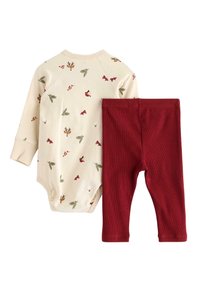 Krämfärgad bodysuit med djur- och växtmotiv, kombinerad med röda rippade leggings. Mjuk bomullsmaterial, tajt passform och långa ärmar.