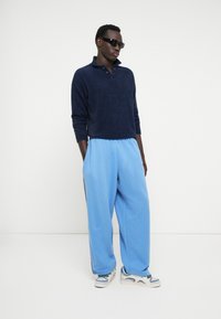 Marineblauer, flauschiger Pullover mit Kragen, kombiniert mit hellblauen, locker sitzenden Hosen mit Seitenstreifen und einer glatten Textur, ergänzt durch Sneakers.