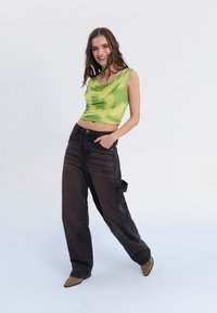 Roheline tie-dye stiilis lühike topp drapeeritud kaelusega, koos mustade laia säärega teksadega, millel on küljetaskud ja kõrge vöökoht.