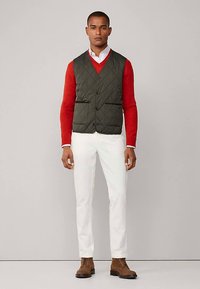 Gewatteerd donkergroen vest, rood shirt met lange mouwen, witte broek en bruine laarzen. Voorzien van knopen aan de voorkant en zijzakken.