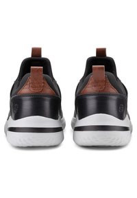 Scarpe sportive nere con dettagli in pelle marrone, dotate di una tomaia in tessuto testurizzato, una suola in gomma bianca e un'etichetta sul retro.