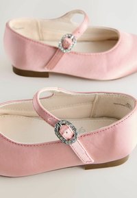Ružové saténové balerínky s zaoblenou špičkou a plochou gumovou podrážkou. Majú ozdobnú pracku s kryštálikmi na nastaviteľnom remienku.