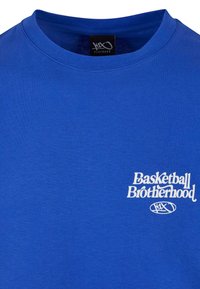 Zila kokvilnas T-kreklu ar apaļu kakla izgriezumu un īsām piedurknēm. Uz tā ar baltu tekstu ir rakstīts "Basketbola brālība" ar logotipu zem tā.
