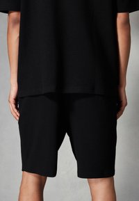 T-shirt noire ample en tissu gaufré avec un ourlet arrondi, assorti à un short noir de longueur genou. Design simple et minimaliste.