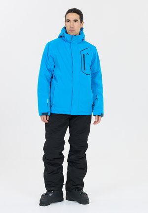 Blå isolerad jacka med ficka med dragkedja på bröstet och justerbar huva, kombinerad med svarta snöbyxor och svarta stövlar. Slät textur, funktionell design.