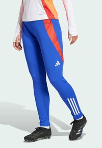 Blaue Sportleggings mit einem roten diagonalen Streifen, aus glattem Material hergestellt; verfügen über drei weiße Streifen am Unterschenkel und ein enganliegendes Design.