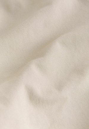 Flødefarvet stof med en glat, blød tekstur, der har subtile rynker og folder, som fremhæver dets lette og fleksible karakter.