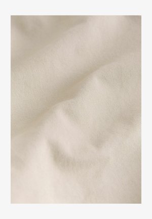 Tela de color crema con una textura suave y lisa, que presenta arrugas y pliegues sutiles, destacando su naturaleza ligera y flexible.