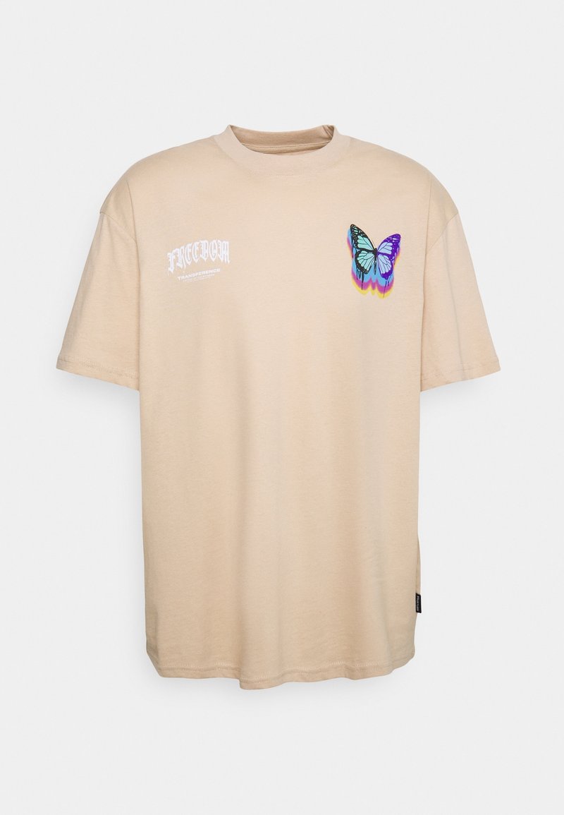 T-shirt beige à manches courtes avec le texte blanc « FREEDOM » et un motif coloré de papillon bleu et violet sur la poitrine.
