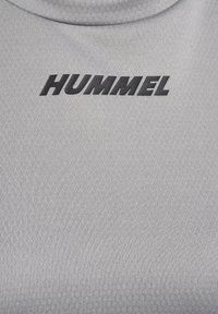Szara sportowa koszulka o teksturowanej powierzchni i wysokim kołnierzu z czarnym logo "HUMMEL" na przodzie.