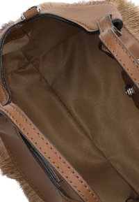 Interieur van een bruine leren handtas met een gladde stofvoering, voorzien van een klein vak en contrasterende stiksels langs de randen.