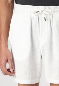 Shorts blancs à texture gaufrée avec une taille élastique et un cordon de serrage, dotés de poches latérales et d'un ourlet replié.