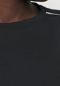 Svart atletisk t-shirt med en slät textur, som har rund halsringning och tunna vita accentränder på axlarna.