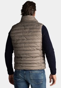 Beige puffer vest met een quilted ontwerp, hoge kraag en mouwloos stijl, gecombineerd met een marineblauwe gebreide trui en blauwe jeans.