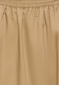 Jupe à taille élastique beige avec de légers plis et un tissu fluide et doux.