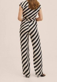 Pruhovaný overal s krátkými rukávy, se diagonálními černými a krémovými pruhy, širokými nohavicemi a páskem v pase. Hladká textura látky.