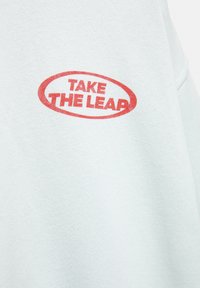 Vaaleansininen huppari, jossa on punainen soikea graafinen kuvio, jossa lukee "TAKE THE LEAP" lihavalla fontilla. Pehmeä, tekstuuriltaan miellyttävä kangas rentoa leikkuuta.