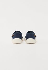 Námornícke slip-on topánky s hladkým textilným zvrškom a bielou gumovou podrážkou. Obsahujú zadný popruh a malý béžový akcent s logom.