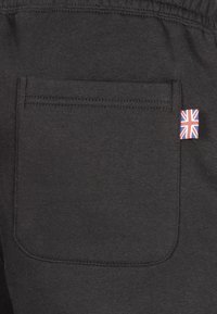 Black fabric pocket with visible stitching. Small Union Jack flag accent on the side. Smooth texture, rectangular shape.