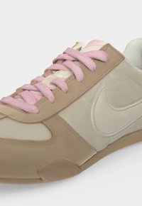 Μπεζ και εκρού αθλητικό παπούτσι Nike με ροζ κορδόνια και λευκό λογότυπο Nike στην πλευρά.