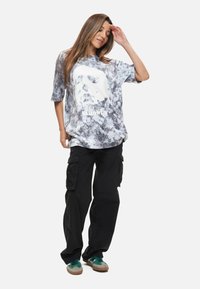 Grå tie-dye t-shirt med en vit Halloween-grafik, kombinerad med svarta cargobyxor och gröna sneakers. Avslappnad passform.