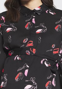 Svart blus med blommönster i röd och rosa. Krage med en knytinredetalj och slät tygtextur.