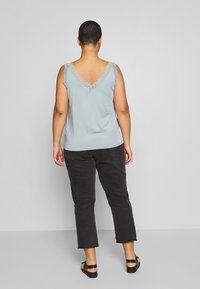 Ljusblå topp med spetsdetaljer vid halsringning och axelkant, kombinerad med svarta cropped jeans och svarta sandaler.