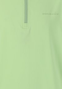 Ljust grön atletisk polo-shirt med halvvindkrage, mjukt tyg och ordet "ENDURANCE" tryckt i en subtil typografi.