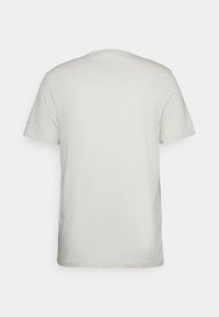 Camiseta de manga corta en beige claro. Cuello redondo, textura suave y corte estándar. Sin gráficos ni patrones visibles.