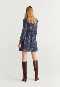 Robe à motif floral bleu foncé, avec des manches à volants, une taille élastique et une jupe à volants. Associée à des bottes bordeaux montantes jusqu'aux genoux.