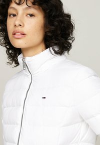Giacca a vento bianca con colletto alto, chiusura con zip e design a righe orizzontali. Presenta un piccolo logo sul petto.