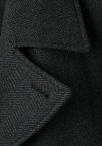 Tela gris oscuro con patrón pata de gallo y acabado texturizado, con cuello doblado y un único detalle de bolsillo rectangular.