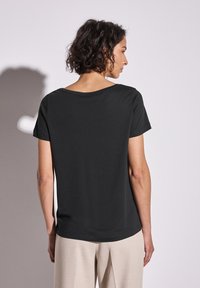 T-shirt noir à manches courtes avec un large col et une coupe décontractée. Tissu lisse et doux avec un design simple et épuré, sans motifs visibles.