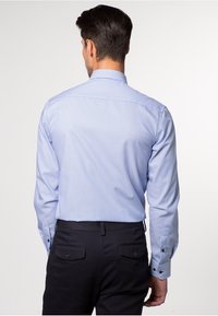 Blau-weiß gestreifte Langarmbluse mit Button-Down-Kragen, strukturiertem Stoff und taillierten Manschetten. Tragen Sie dazu dunkle Hosen, Rückansicht.