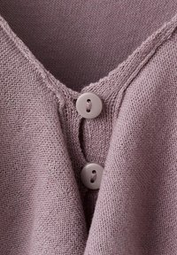 Nahaufnahme eines staubig rosa gestrickten Stoffes mit zwei passenden runden Knöpfen, die entlang eines V-förmigen Ausschnitts befestigt sind.