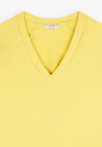 T-shirt giallo a V, realizzato in cotone morbido. Presenta un colletto a costine e una texture con l'etichetta del marchio "SCALPERS" visibile all'interno del colletto.