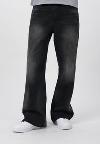 Jeans de mezclilla de pierna ancha en gris oscuro con una textura deslavada, combinados con zapatillas blancas con detalles perforados y suela plana.