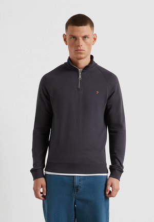 Maglione grigio scuro con zip, colletto e polsini a coste. Presenta un piccolo logo sul petto e una vestibilità comoda, abbinato a jeans blu.