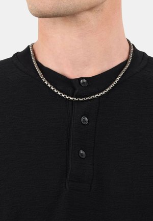 Schwarzes, strukturiertes Henley-Shirt mit drei Knöpfen am Kragen; eine silberne Kette ist um den Hals sichtbar.