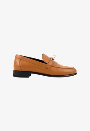 Mocassin homme en cuir marron clair avec semelle noire et détail de boucle métallique argentée sur fond blanc.
