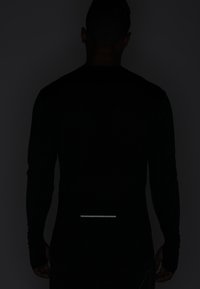 Mężczyzna w czarnej koszulce z długim rękawem pokazany od tyłu, z odblaskowym poziomym paskiem w pobliżu dolnej części pleców.