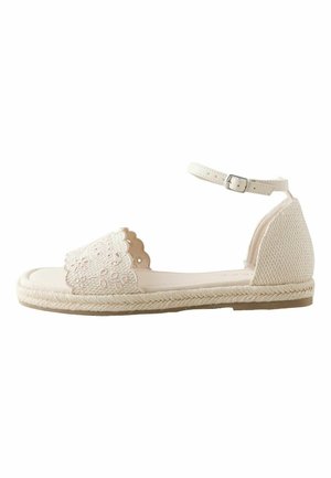 Beige flat sandal with ankle strap, floral eyelet design on front strap, woven jute sole, and textured heel counter.