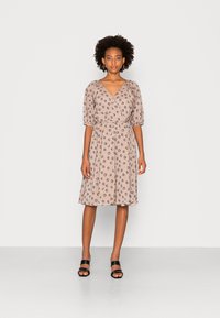 Vestido envolvente floral em tecido bege suave, com mangas bufantes, cintura ajustada e saia até ao joelho. Padrão floral preto por toda a peça.