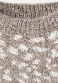 Pull en maille avec une base beige texturée ornée de motifs blancs irréguliers. Encolure côtelée et matériau doux et duveteux.