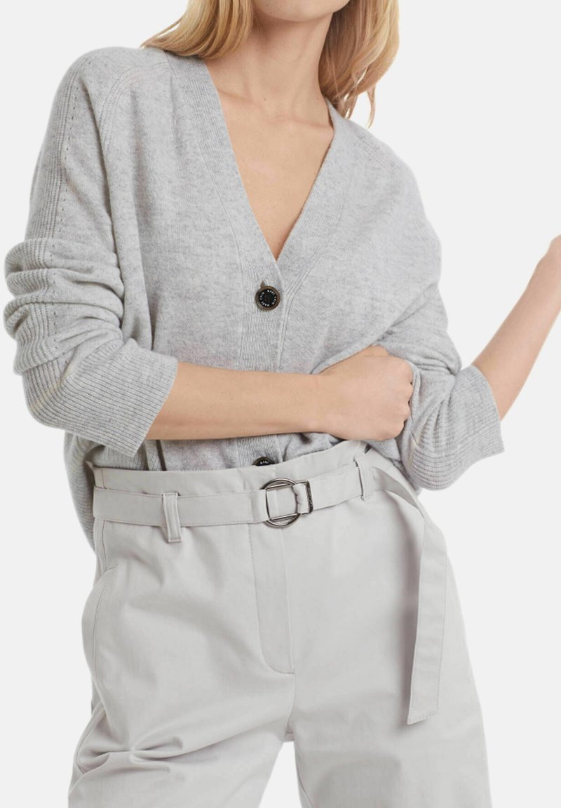 Cardigan gris en maille avec un col en V profond, orné d'un bouton noir. Associé à un pantalon taille haute gris clair et une taille ceinturée.
