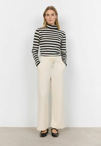 Striped black and white turtleneck top paired with cream wide-leg trousers featuring an elastic waistband and drawstring. Black flats complete the look.