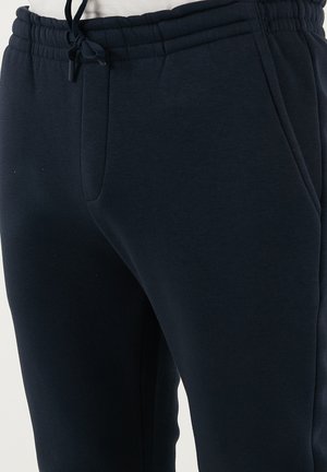 Temno modri trenirki iz mehkega materiala, z elastičnim pasom in vrvico, stranskimi žepi ter oblikovanim nogavice.