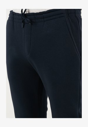 Marineblå sweatpants lavet af blødt stof, med en elastisk talje med snor, sidelommer og et tapered ben-design.